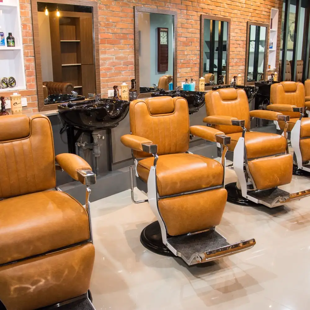 Interior de una barbería con sillones de cuero, espejos y paredes de ladrillo
